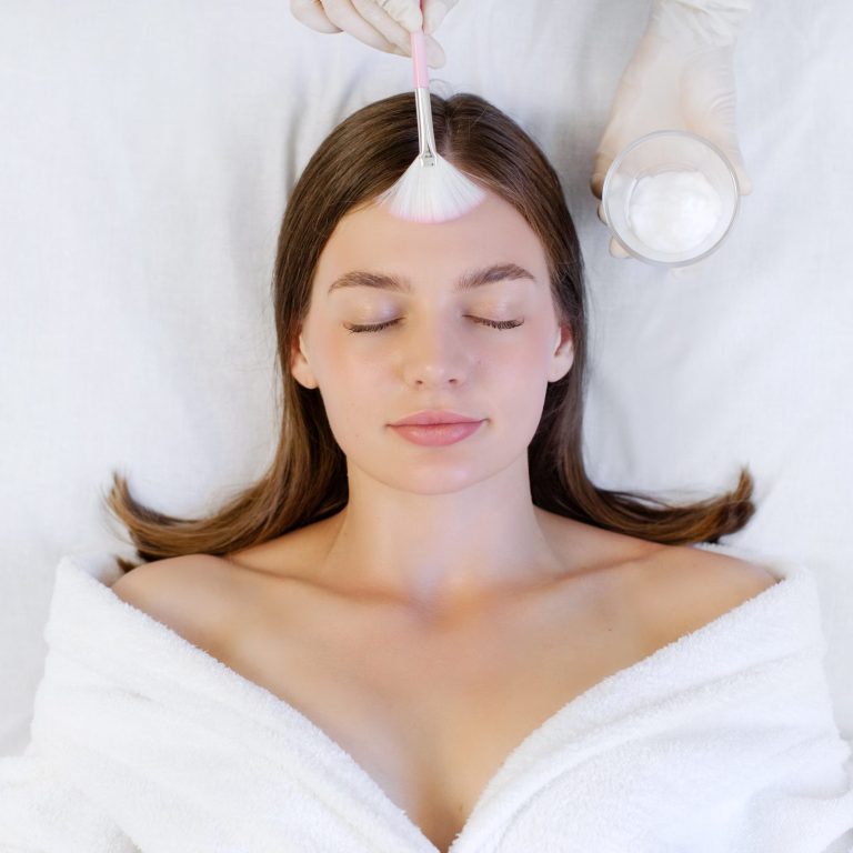 Cosmetic procedure. Doctor's hand with brush touching face of young beautiful woman, doing chemical peeling. Facial skin care concept